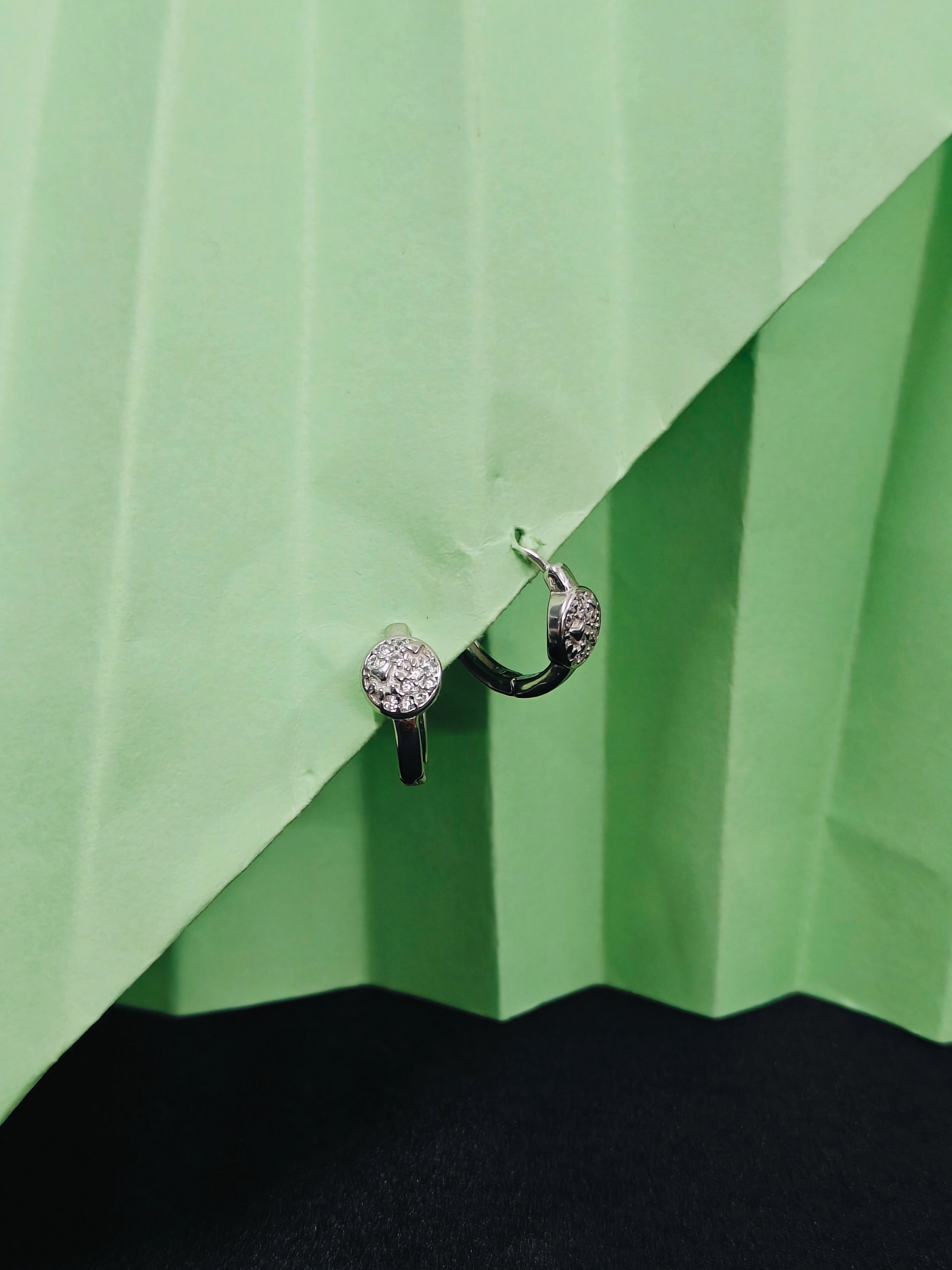 Pair of earrings on a green pleated fabric background